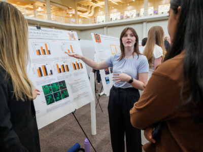 A Mercer student gestures to her research posters as she talks to two people.