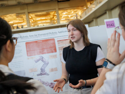 A Mercer student explains her research poster about a robotic arm to two other people.