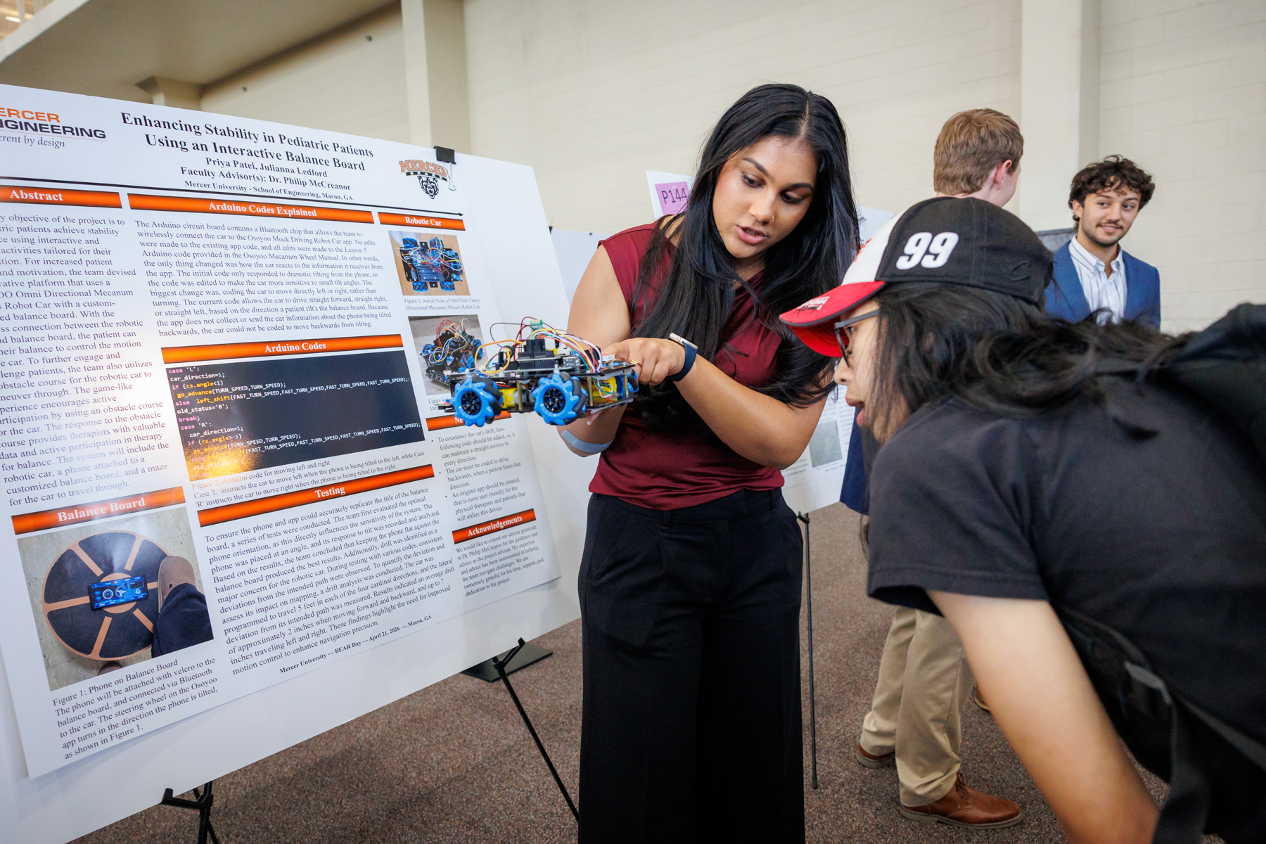 A Mercer student points to something on a handheld robotic car and another student leans in close to see.