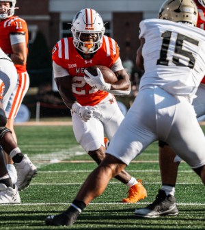 Mercer football player #25 in orange runs with the ball toward a defender in white and gold during a home game.