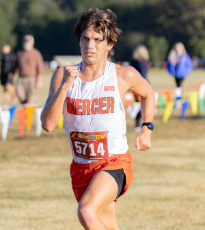 Mercer University cross country runner #5714 competes in a race across an open grass course on a sunny day.