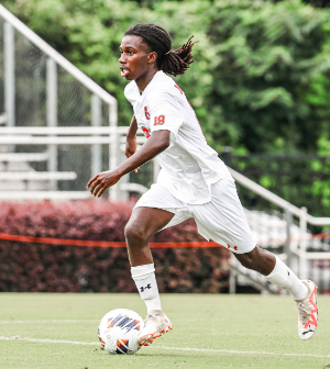 Mercer men's soccer player #19 in a white jersey dribbles the ball downfield during a match.