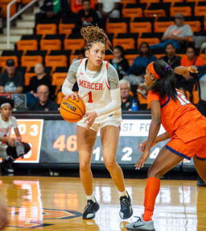 Mercer women's basketball player #1 dribbles and looks to make a move past a defender in orange during a home game.