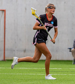 A Mercer women's lacrosse player in a black jersey runs with the ball in her stick during a match.