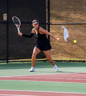 A Mercer women's tennis player in a black outfit reaches to hit a forehand shot during an outdoor match on a sunny day.